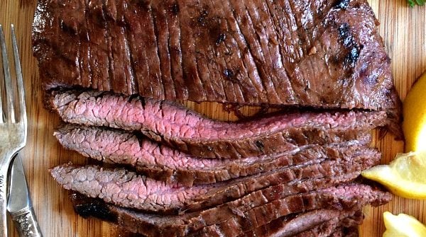 Overhead shot of grilled flank steak, half cut into strips showing off the pink meat inside