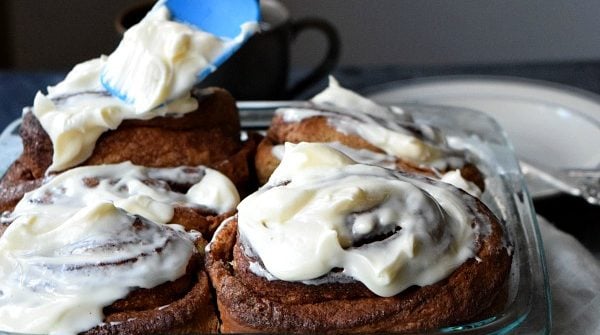 Overnight Gingerbread Cinnamon Rolls being frosted with cream cheese frosting