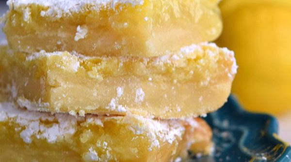 3 gooey lemon squares on a teal plate covered in powdered sugar
