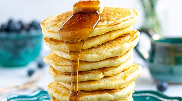 syrup being poured onto a tall stack of pancakes made from scratch
