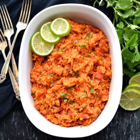overhead shot of mexican rice with limes, cilantro, and forks