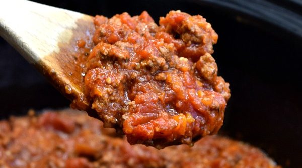 a large spoon full of bolognese sauce over top a crockpot