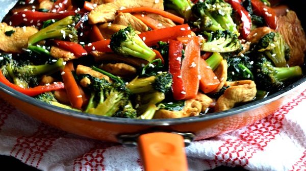 a toddler hand holding the handle of a skillet filled with 20 minute chicken stir fry