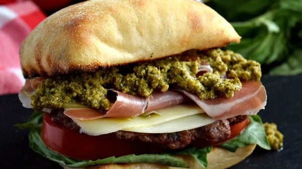 a close up of a prosciutto pesto burger on a black plate with a beer