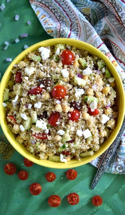 Greek Quinoa Chickpea Salad in a big yellow bowl with a napkin on a green background