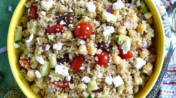 Greek Quinoa Chickpea Salad in a big yellow bowl with a napkin on a green background