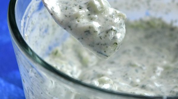 A spoonful of Easy Homemade Tzatziki Sauce Recipe dripping into the bowl