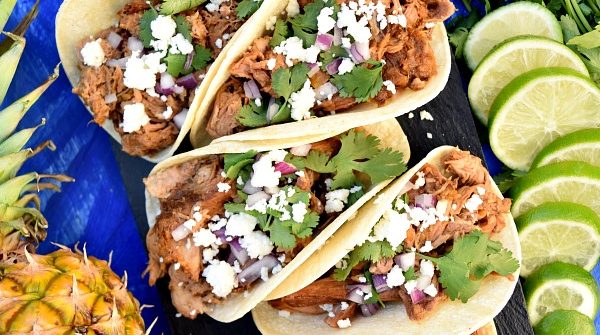 Slow Cooker Chipotle Pineapple Carnitas on a serving platter topped with cheese, onions, and cilantro