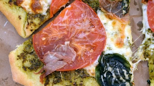 a slice of Pesto Pizza with Prosciutto, Tomatoes, and Mozzarella