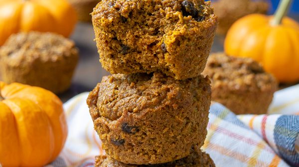 Pumpkin Bran Muffins stacked on a plaid towel, the top one has a bite taken out