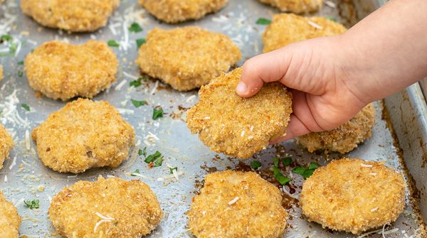 a toddler hand holding a baked chicken nugget