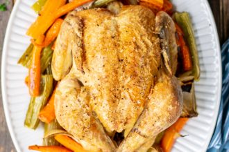 whole roasted chicken on a bed of veggies on a white platter