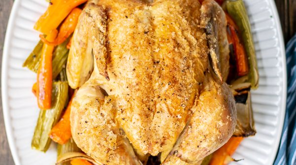 whole roasted chicken on a bed of veggies on a white platter