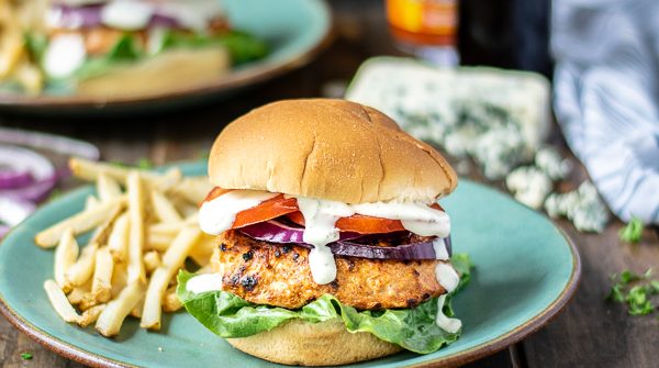 a stuffed chicken burger on a teal plate with French fries on a table