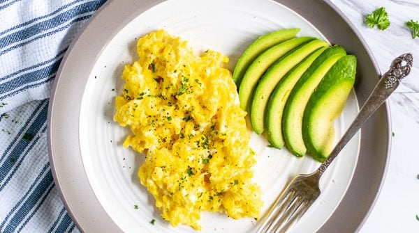 cottage cheese scrambled eggs and sliced avocado on a plate with a fork