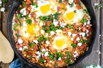 overhead shot of shakshuka in a cast iron skillet on a wood table with a blue striped towel