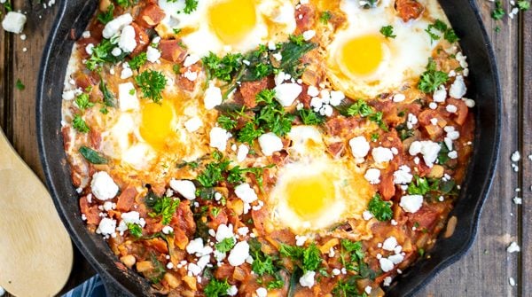 overhead shot of shakshuka in a cast iron skillet on a wood table with a blue striped towel