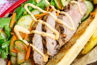 a flavorful grilled pork banh mi in a serving basket with quick pickled vegetables, sriracha mayo, and cilantro
