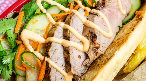 a flavorful grilled pork banh mi in a serving basket with quick pickled vegetables, sriracha mayo, and cilantro