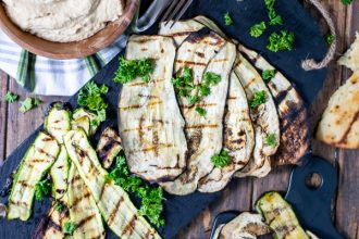a spread of grilled zucchini, eggplant, naan, and hummus over a wooden background
