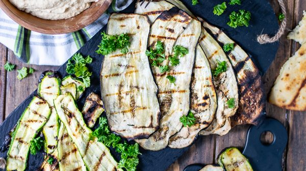 a spread of grilled zucchini, eggplant, naan, and hummus over a wooden background