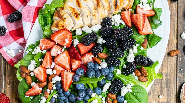 overhead view of a summer berry salad on a large platter with a napkin and a lot of berries