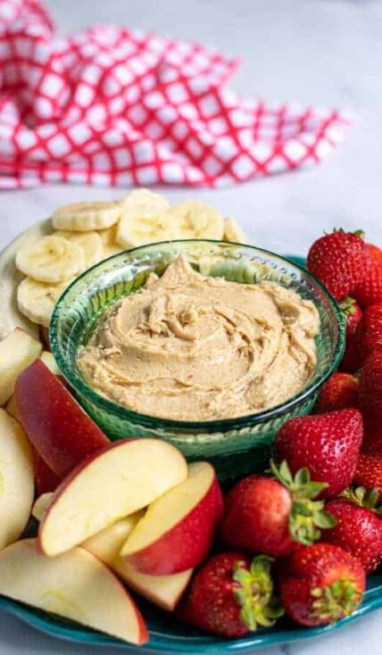 Platter with peanut butter fruit dip surrounded by cut up fruit.