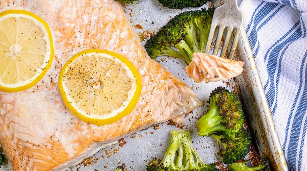 forkful of baked salon with broccoli on a sheet pan