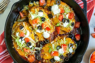 Taco Chicken Breasts in a cast iron skillet with lettuce, tomatoes, sour cream, and black olives