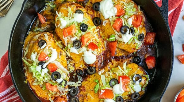Taco Chicken Breasts in a cast iron skillet with lettuce, tomatoes, sour cream, and black olives