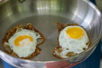person holding a stainless steel frying pan with 2 fried eggs in it