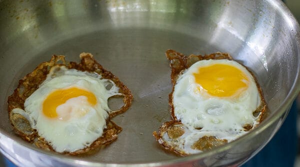 person holding a stainless steel frying pan with 2 fried eggs in it