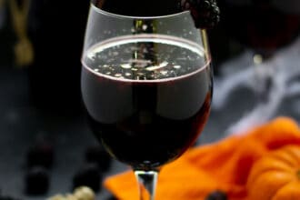 blackberry halloween sangria in a wine glass with fruit and pumpkins and skeletons on the table