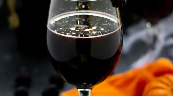 blackberry halloween sangria in a wine glass with fruit and pumpkins and skeletons on the table