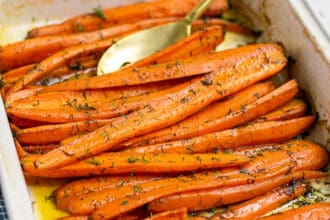 roasted carrots with dill and brown sugar in a white baking dish with a gold spoon
