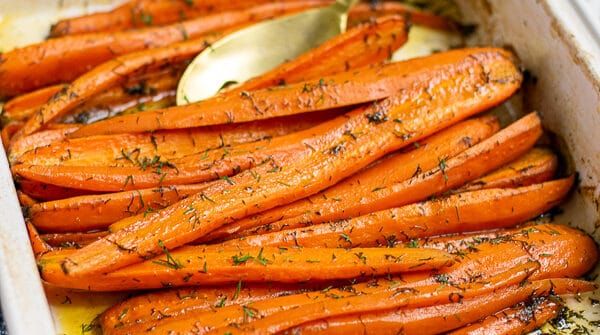 roasted carrots with dill and brown sugar in a white baking dish with a gold spoon