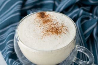 milk steamer drink in a clear mug with cinnamon sprinkled on top