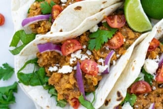three red lentil tacos with vegetarian taco meat on a white plate with garnishes