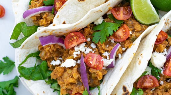 three red lentil tacos with vegetarian taco meat on a white plate with garnishes