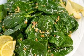 a white platter full of simple spinach salad with cheese and walnuts