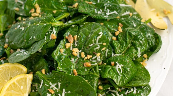 a white platter full of simple spinach salad with cheese and walnuts