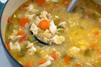 blue dutch oven filled with chicken and rice soup with a ladle full of soup