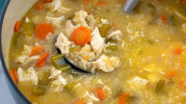 blue dutch oven filled with chicken and rice soup with a ladle full of soup