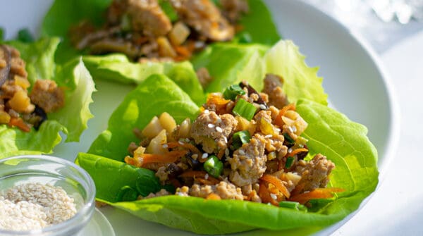 a white plate full of asian chicken lettuce wraps with sesame seeds and green onions