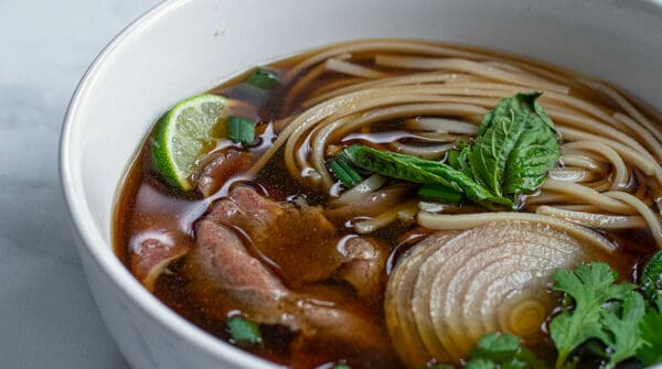 bowl of beef pho made in the slow cooker covered in green garnishes are ready to eat