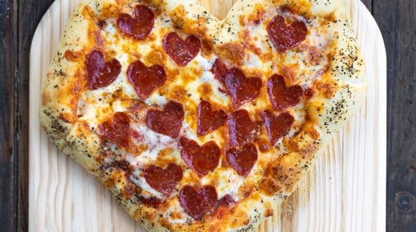 a freshly baked heart shaped pizza on a pizza paddle with heart shaped pepperoni