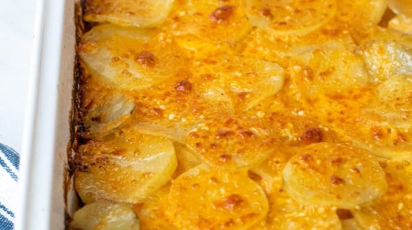 hands with towels holding a freshly made casserole full of Au Gratin Potatoes