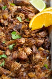 close up photo showing crispy carnitas on a sheet pan with an orange slice