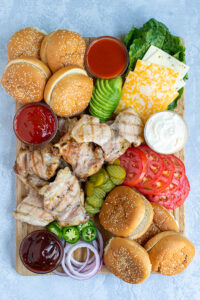 grilled chicken sandwich board filled with a variety of sauce, garnishes, buns, and grilled chicken