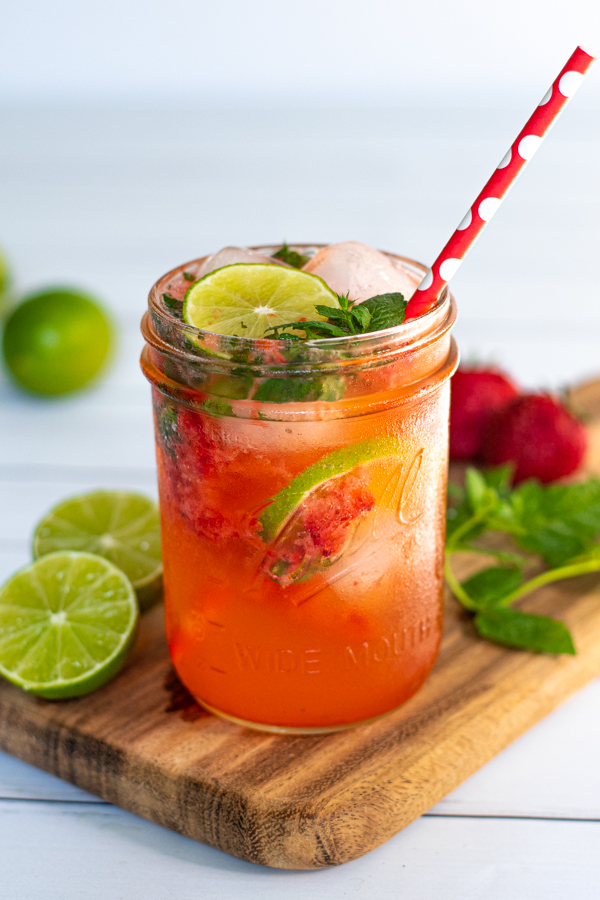 drinking glass jar filled with a bright pink Strawberry Mojito Mocktail made with lime seltzer and garnished with lime slices and fresh mint leaves